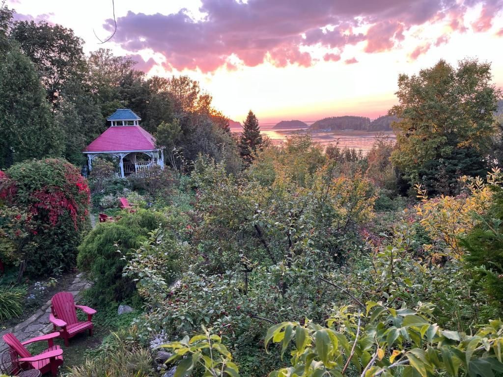 Een weelderige tuin bij zonsondergang met een roze prieel, rode stoelen en een kleurrijke hemel boven de heuvels in de verte.