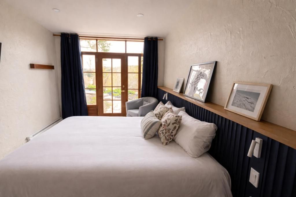 Gezellige slaapkamer met een groot bed, donkere gordijnen, ingelijste kunst en glazen deuren naar een balkon.