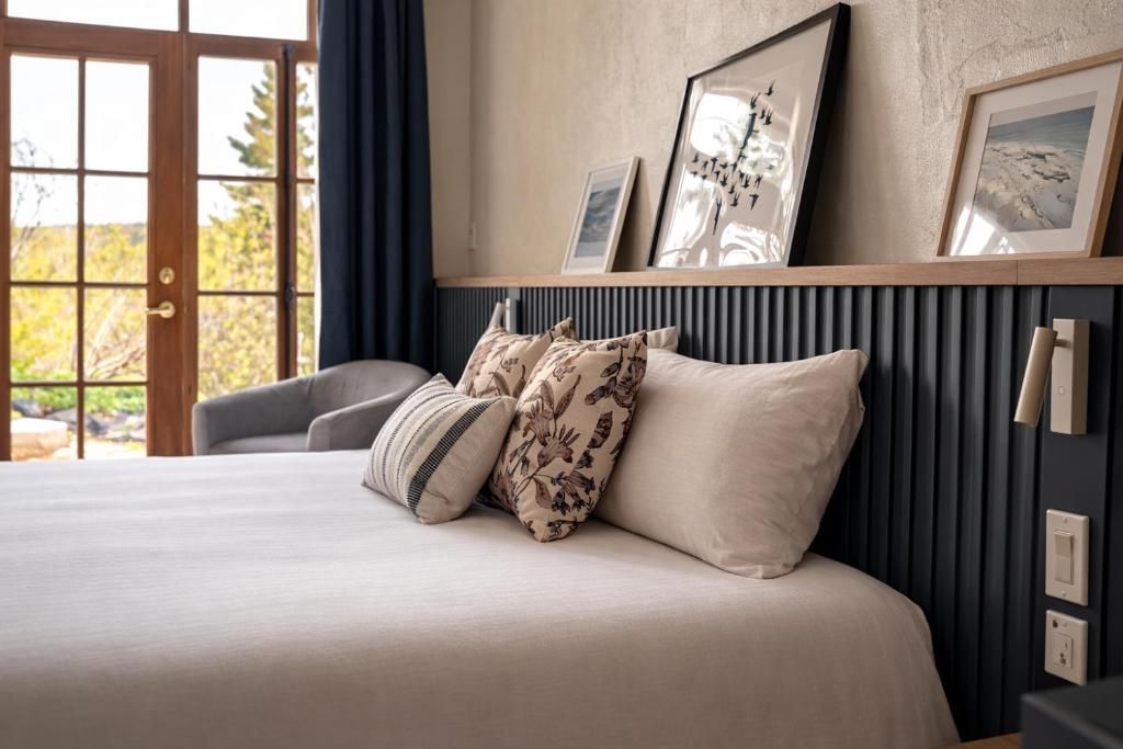 Moderne slaapkamer met een netjes opgemaakt bed, een donkerhouten hoofdeinde en ingelijste kunst bij het raam.
