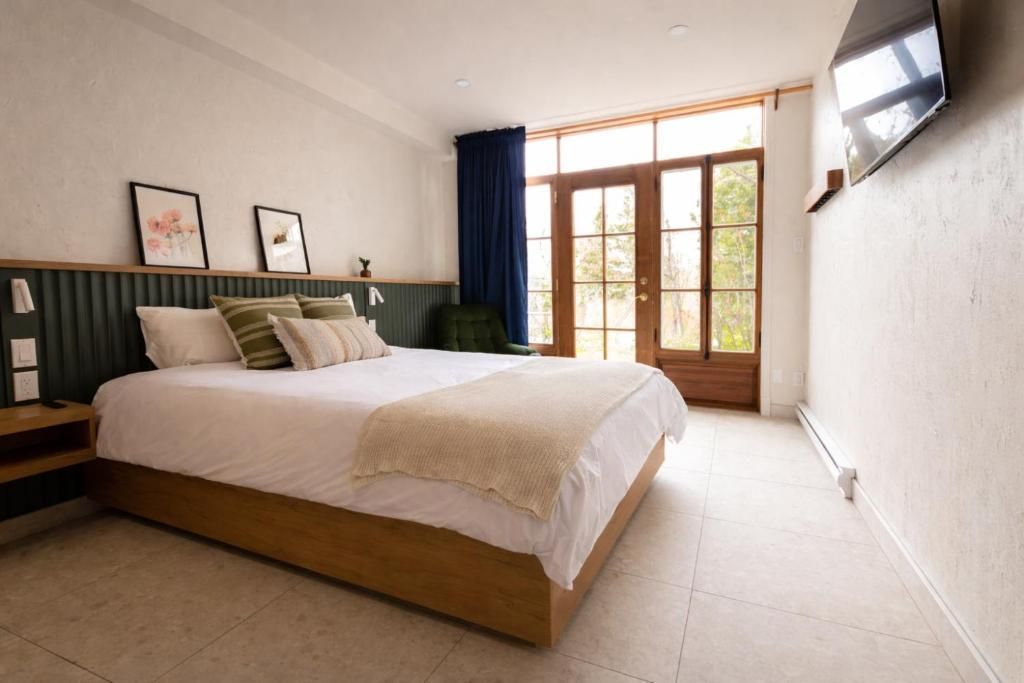 Moderne slaapkamer met een bed, donkergroen hoofdbord, tv aan de muur en openslaande deuren naar het balkon die natuurlijk licht binnenlaten.