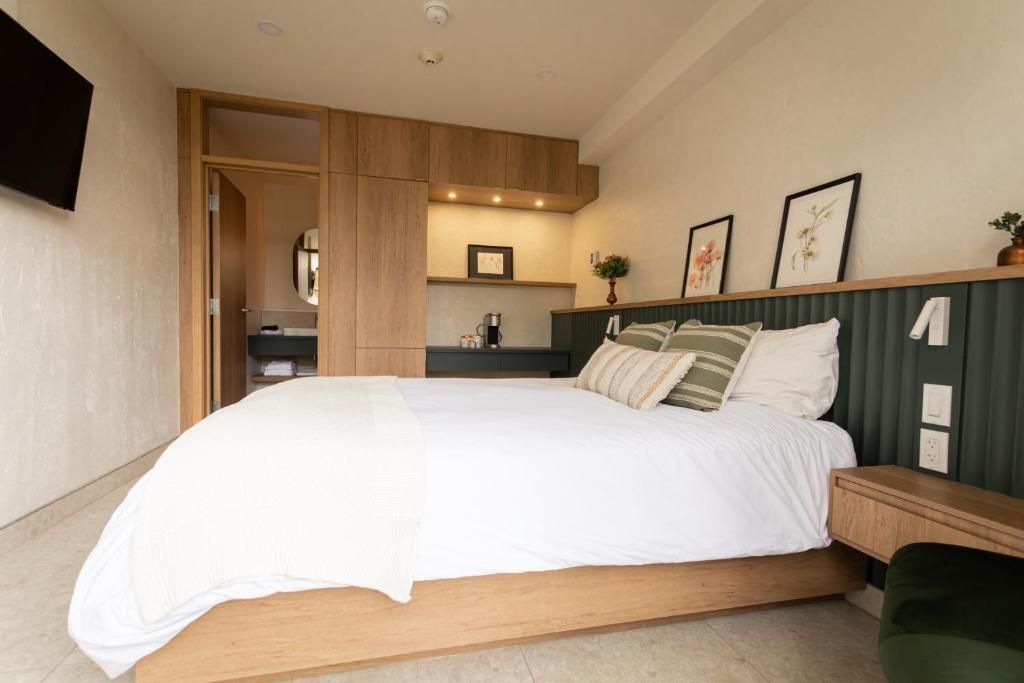 Moderne slaapkamer met een groot wit bed, houten accenten en een kleine kitchenette op de achtergrond.