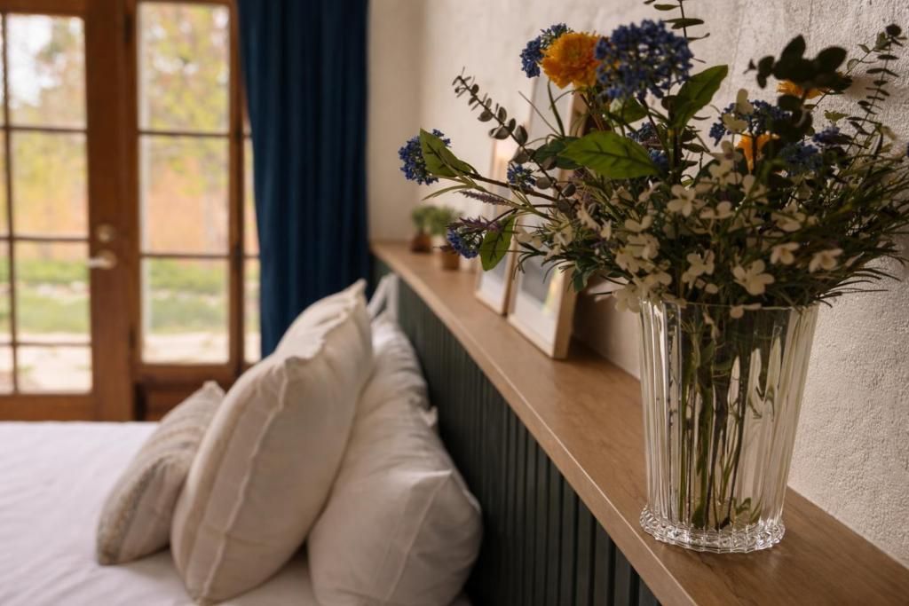 Bloempotten op een houten plank naast een gezellige vensterbank met witte kussens en gordijnen.