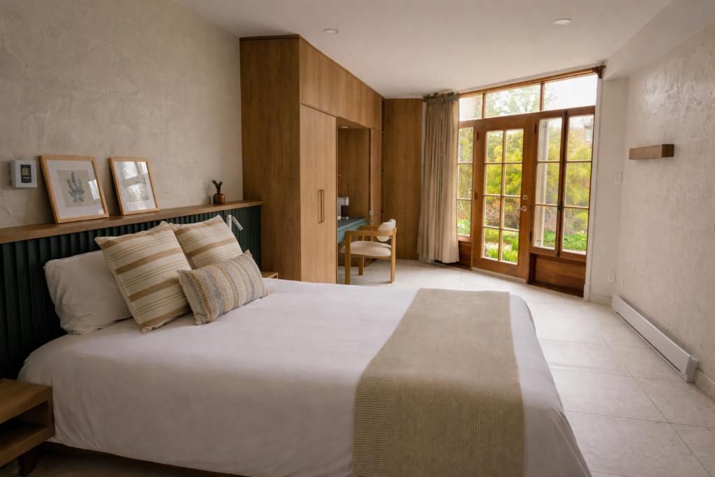 Lichte slaapkamer met een bed, ingebouwde houten planken en grote glazen deuren die uitkijken op groen.