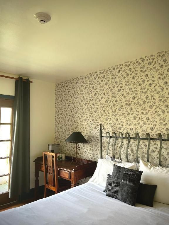 Gezellige slaapkamer met bloemenbehang, ijzeren bed, bureau, groene gordijnen en raamlicht.