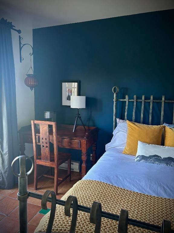 Gezellige slaapkamer met een turquoise muur, messing bed, houten bureau, stoel, lamp en lichtblauw beddengoed.