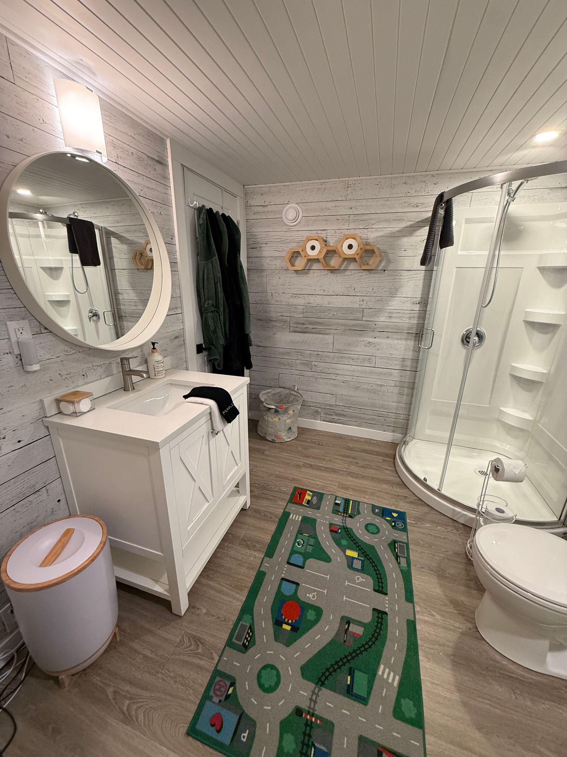 Lichtwitte badkamer in een dome tent van Balsam Ridge Forest Domes met ronde spiegels, wastafel op een voetstuk, douche, toilet en een badmat op de vloer.