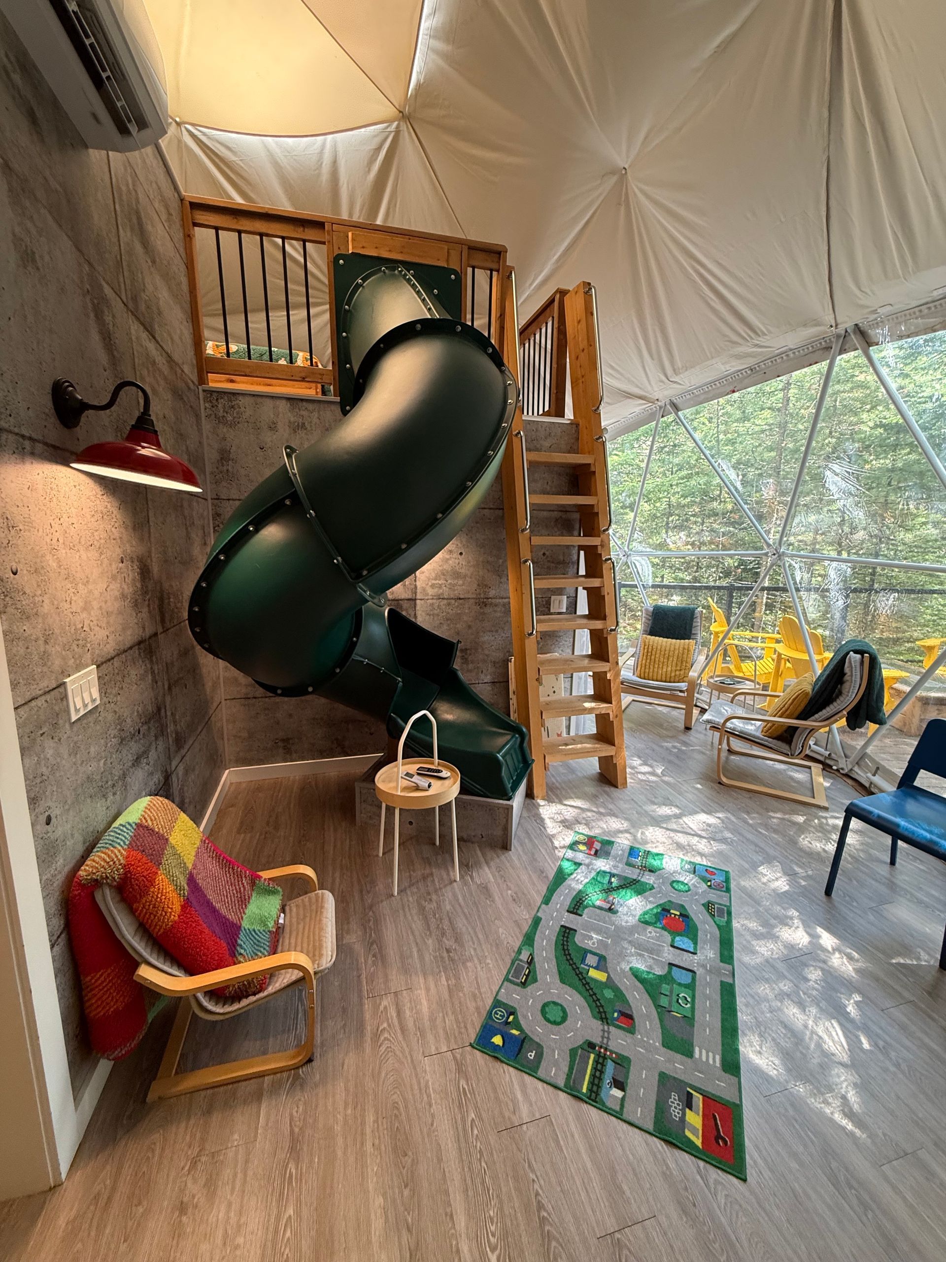 Woonkamer in een dome tent van Balsam Ridge Forest Domes met zwarte spiraalglijbaan, ladder op het mezzanine, kleurrijke stoel en een patroonkleed.