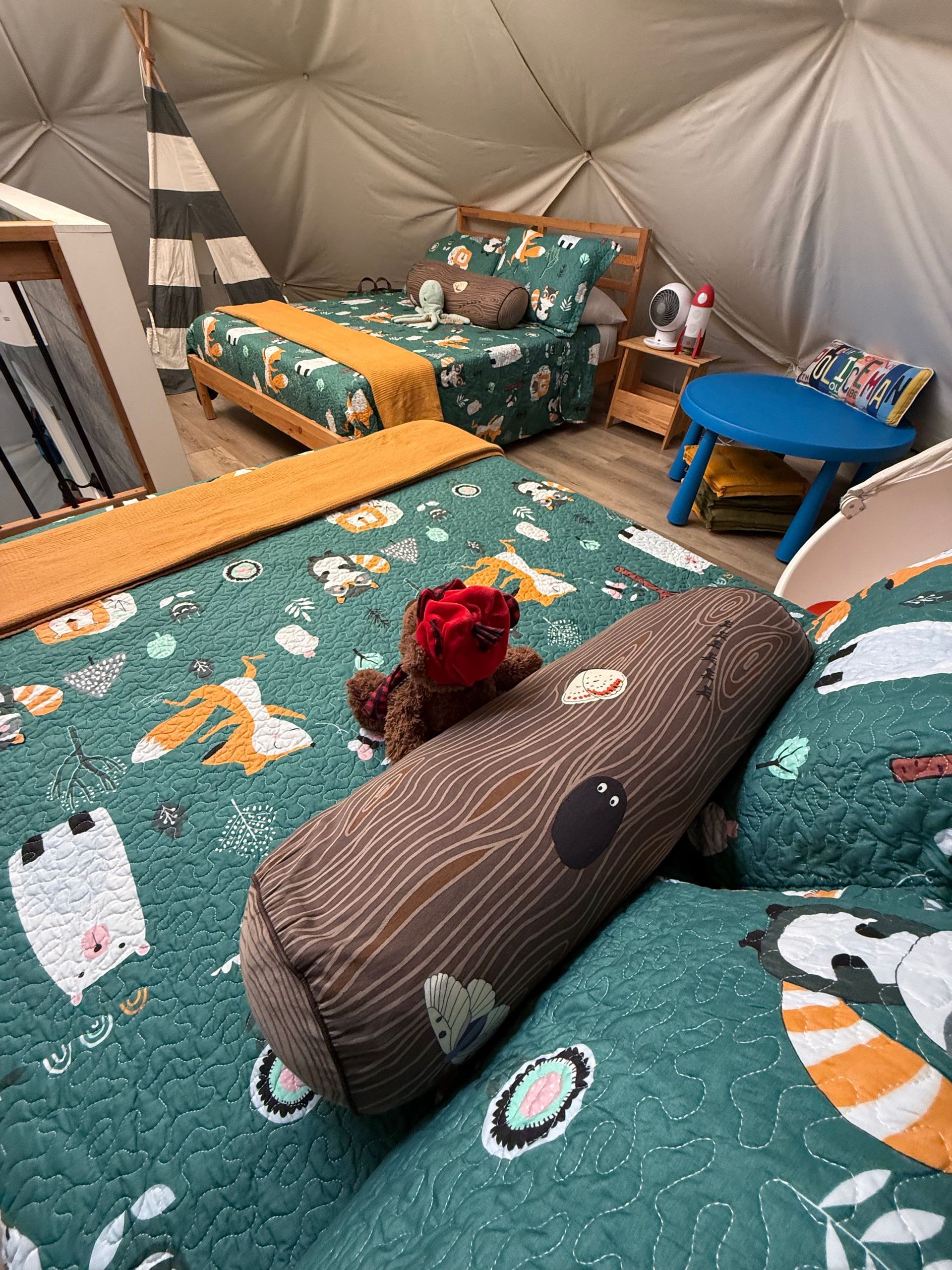 Gezellige zithoek in een dome tent van Balsam Ridge Forest Domes met turquoise kussens met patroon, een grijs sierkussen en een rood bloemstuk in het midden.