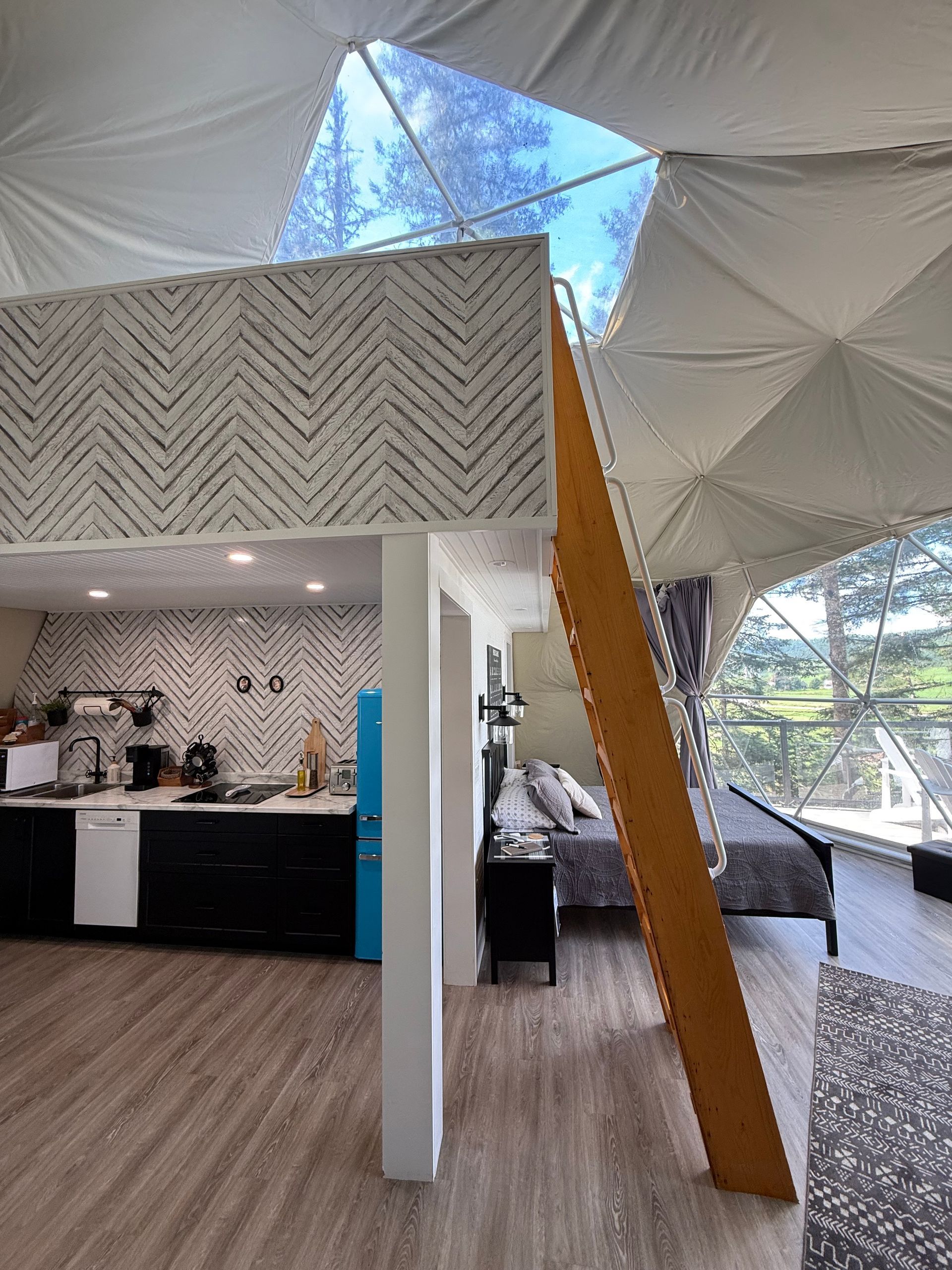 Moderne dome tent van Balsam Ridge Forest Domes met wanden met patroon, een wit koepelplafond en een houten trap/balk.
