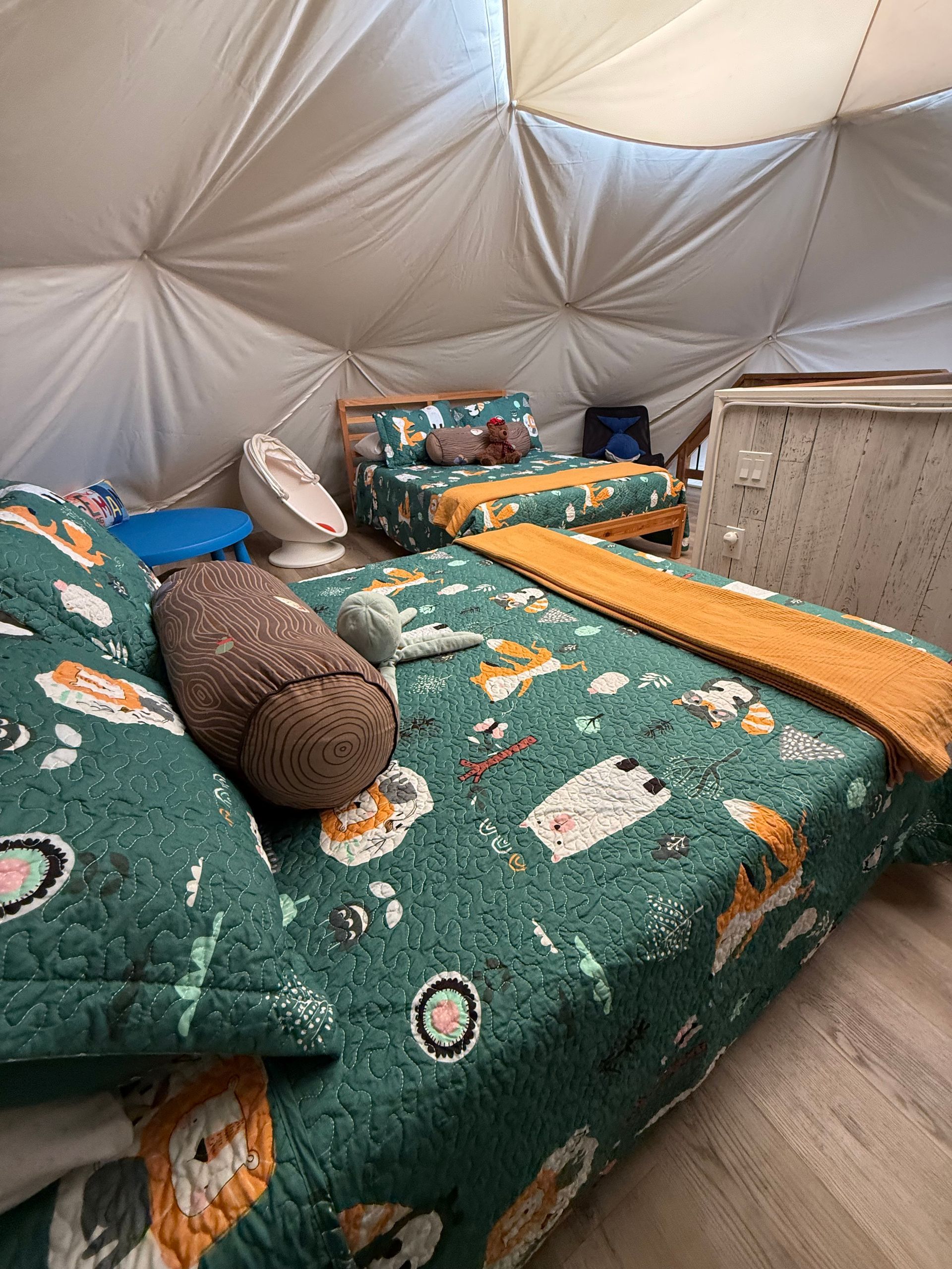 Gezellig bed met groen beddengoed en kussens met patroon in een witte, dome tent van Balsam Ridge Forest Domes.