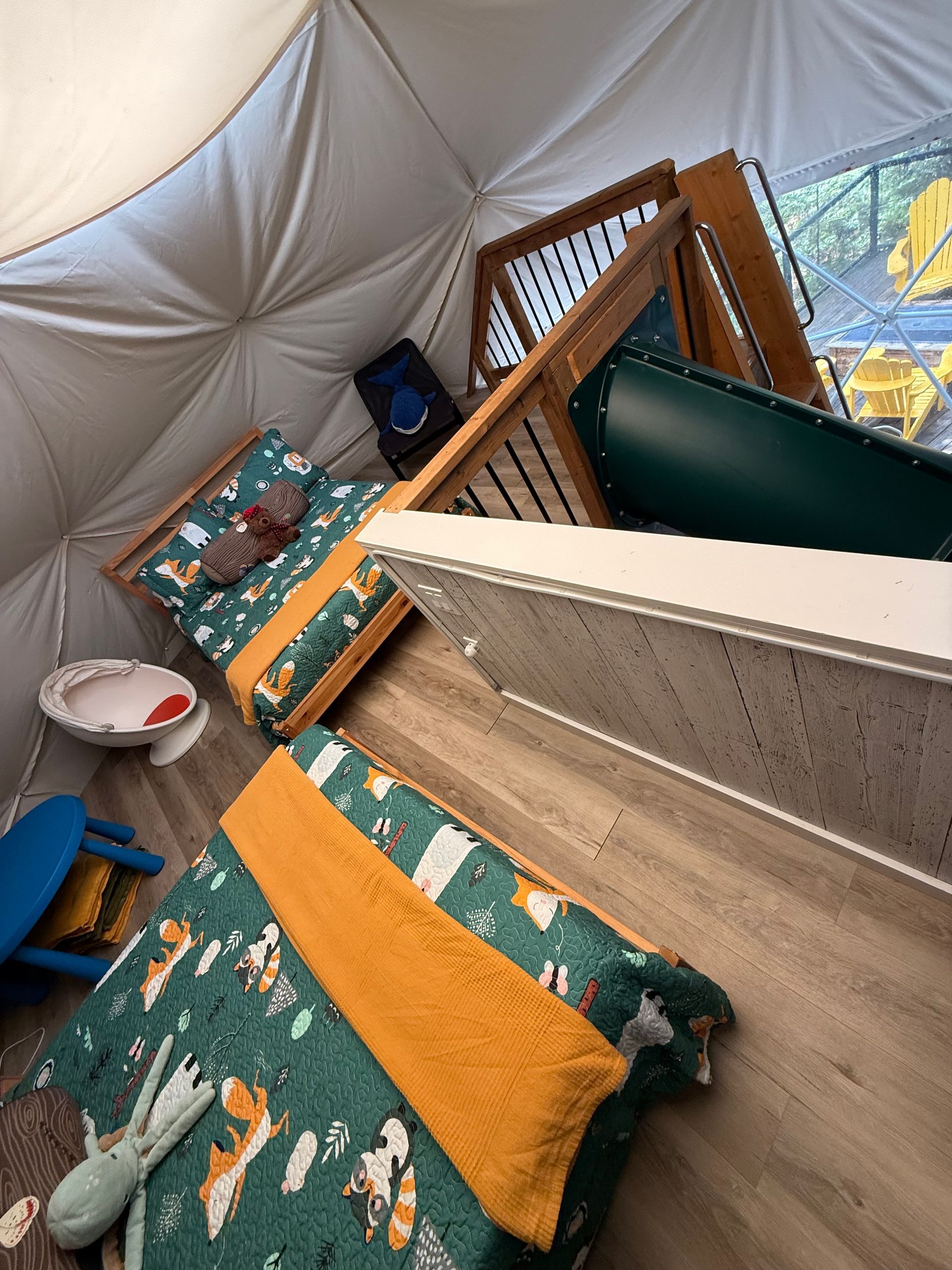 Schuin zicht op een knusse binnentent van een dome tent van Balsam Ridge Forest Domes met dekens met patronen, kussens, een stoel en een wieg of box.