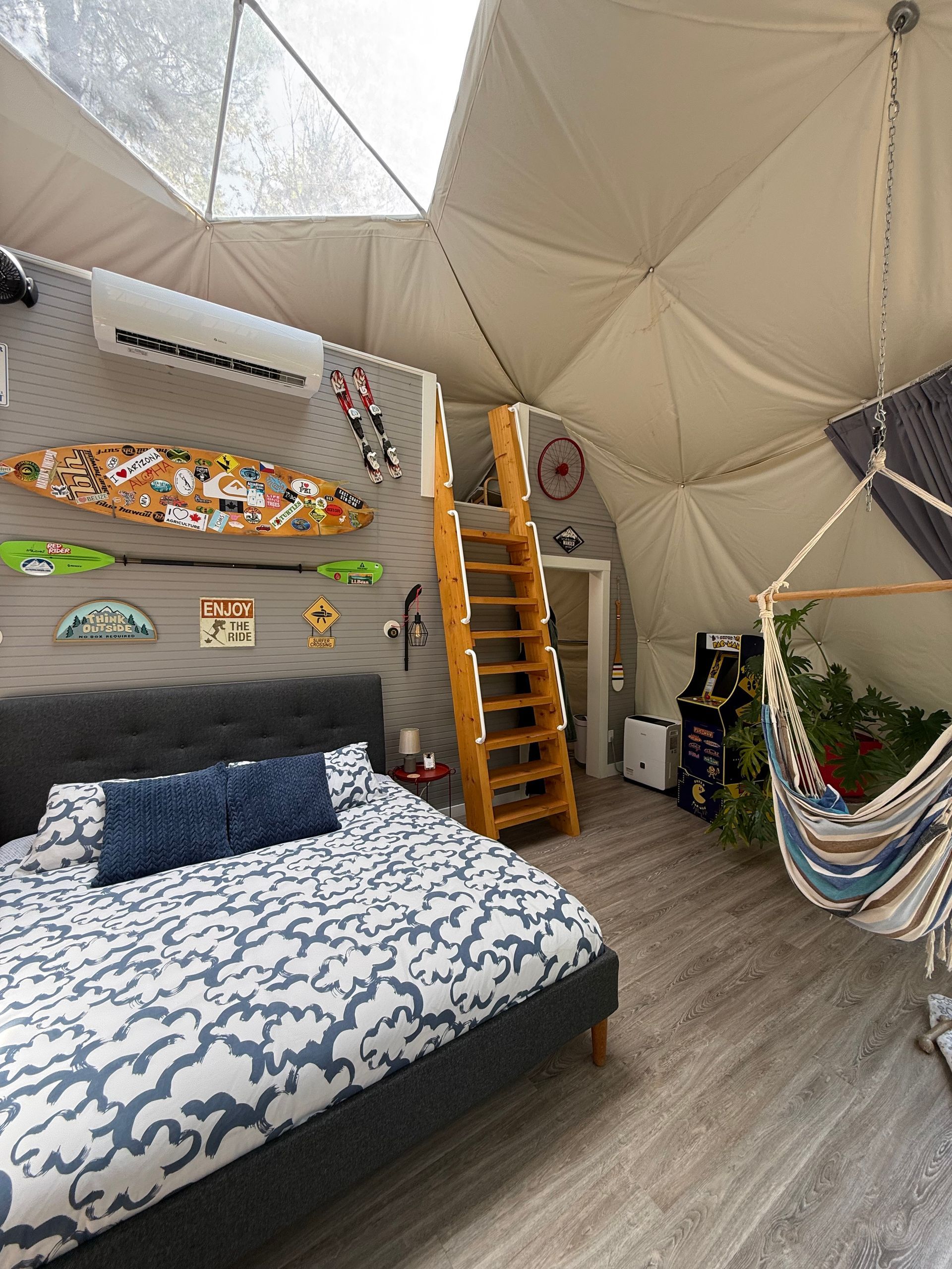 Gezellige slaapkamer in een geodetische dome tent van Balsam Ridge Forest Domes met een bed, houten trap en kleurrijke wanddecoratie.
