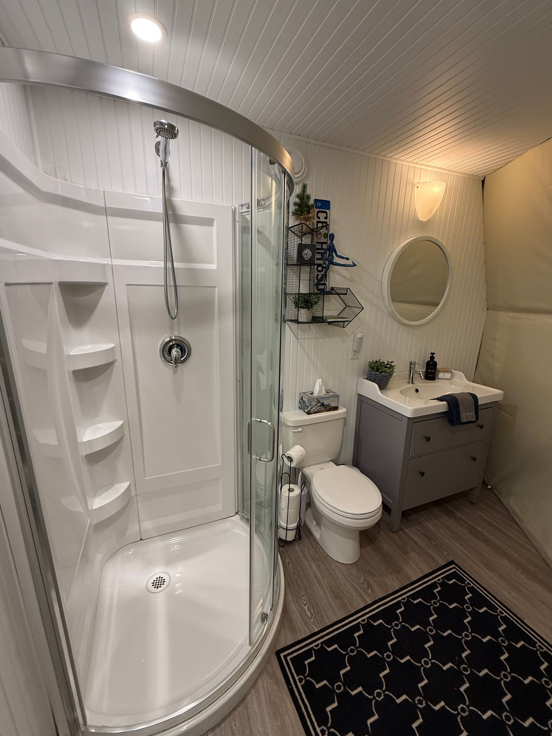 Compacte badkamer in een dome tent van Balsam Ridge Forest Domes met gebogen douche, toilet, wastafelmeubel, ronde spiegel en zwart patroonkleed.