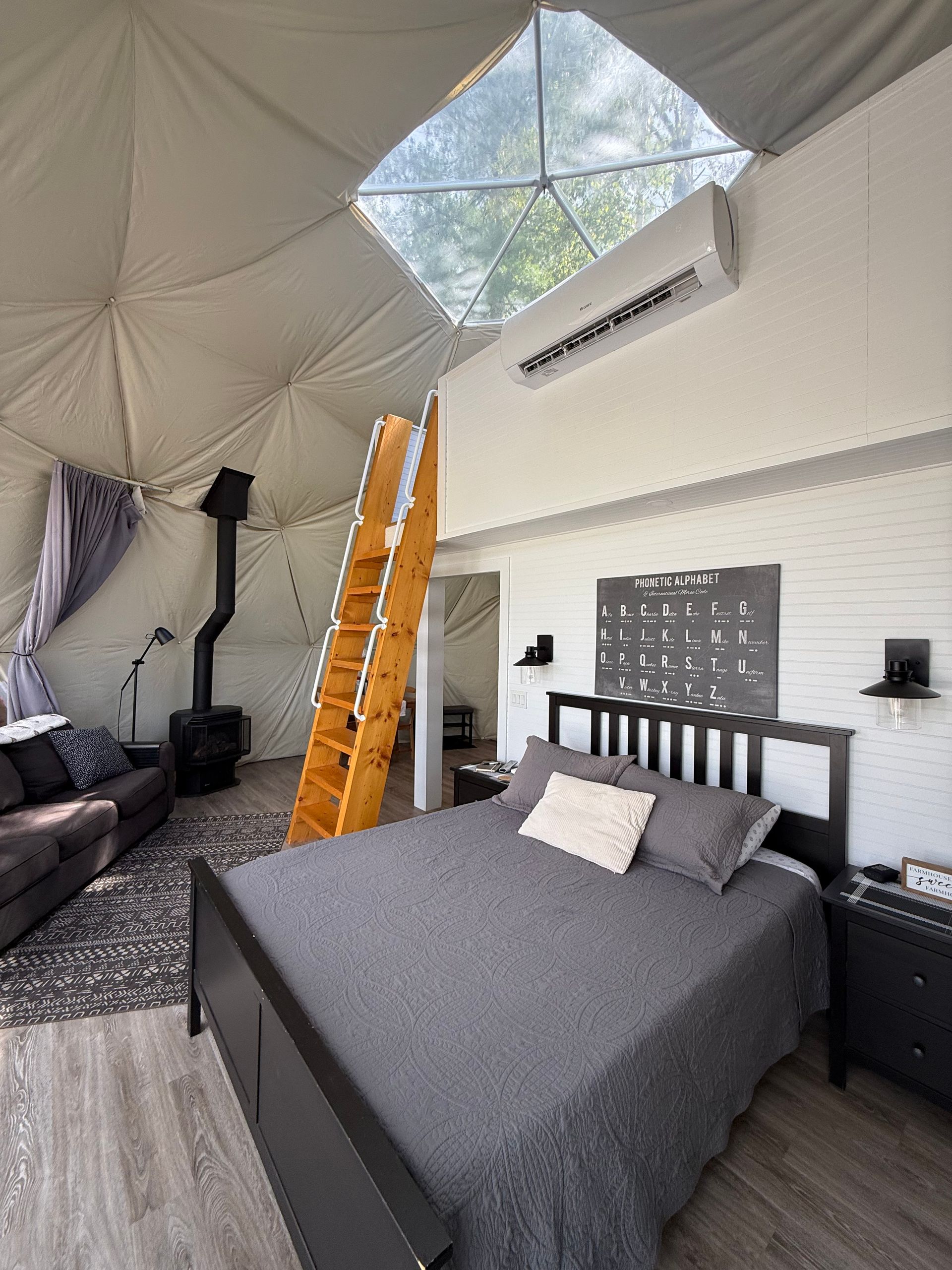Moderne slaapkamer in een dome tent van Balsam Ridge Forest Domes met een zwart bed, oranje ladder en dakraam.