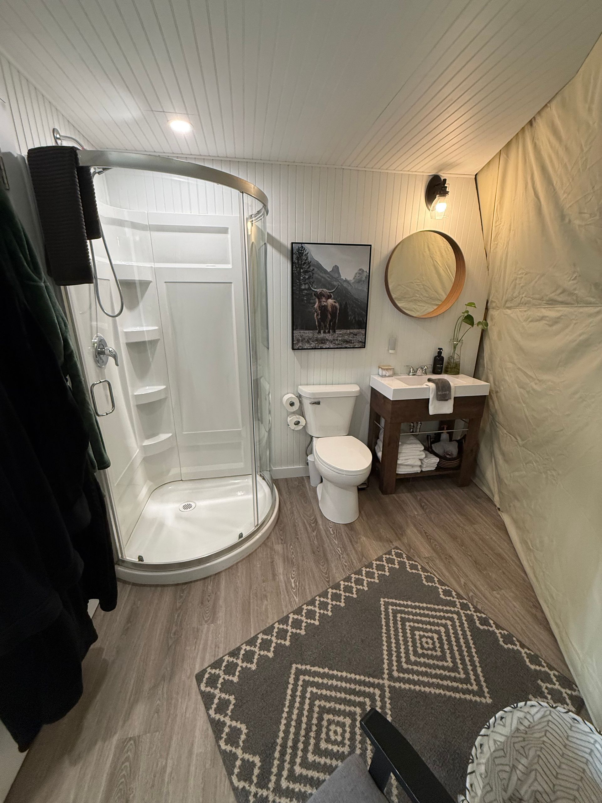 Badkamer in een dome tent van Balsam Ridge Forest Domes met douchecabine, toilet, wastafel, spiegel en een vloerkleed met patroon, verlicht door sfeervolle lampen.