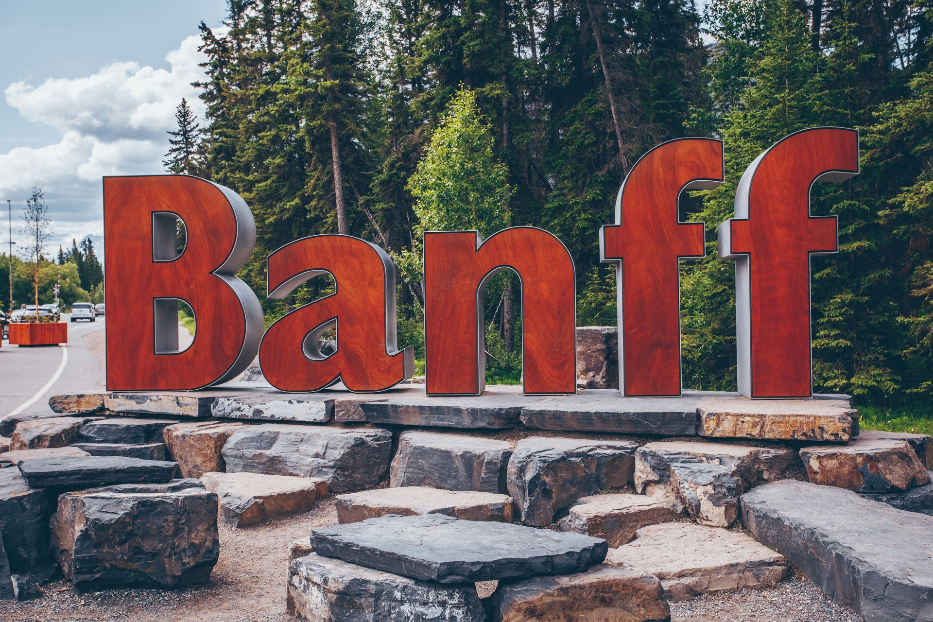 Rood Banff-bord op een stenen sokkel met groenblijvende bomen en bergen op de achtergrond.