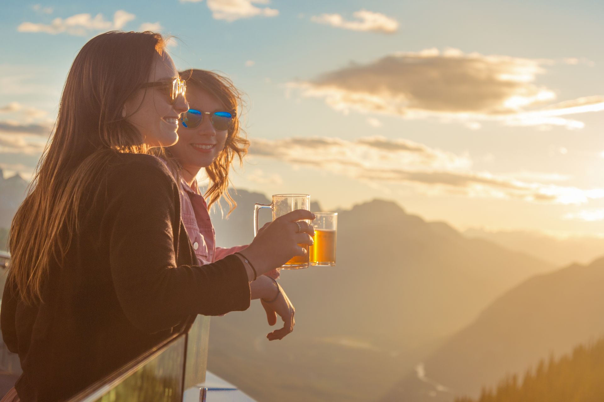 Twee mensen genieten met een drankje van het uitzicht op de zonsondergang boven de bergen vanaf een balkon in Banff National  Park.