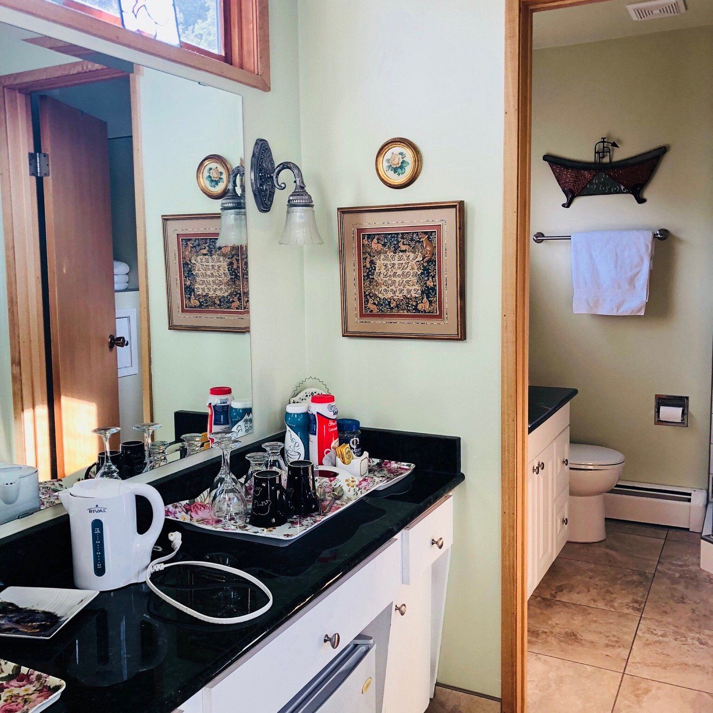 Badkamermeubel met zwart aanrechtblad, spiegel, wastafel, handdoekrek en toilet op de achtergrond.