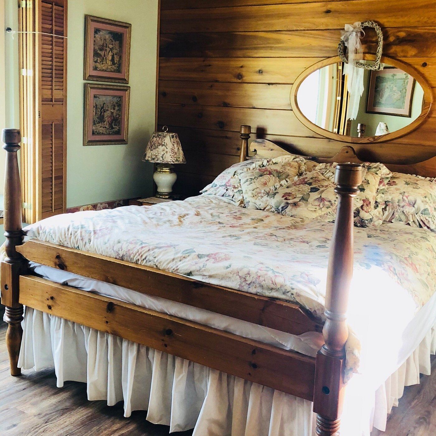 Rustieke slaapkamer met houten bed, bloemenbeddengoed, ovale spiegel en zacht natuurlijk licht.