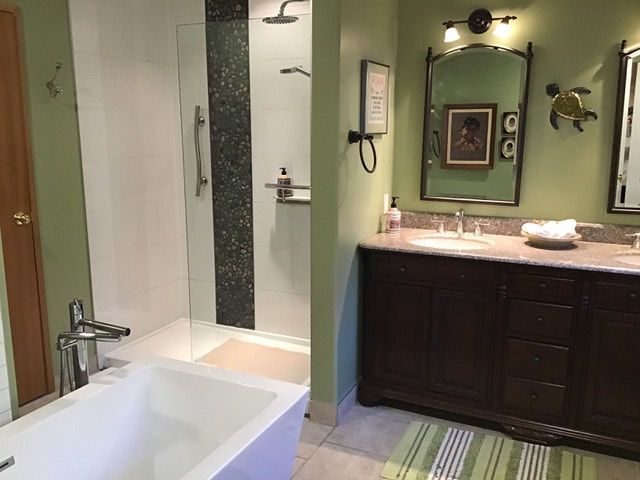 Moderne badkamer met een wit bad, glazen douchecabine en een donkerhouten wastafelmeubel met groene muren.