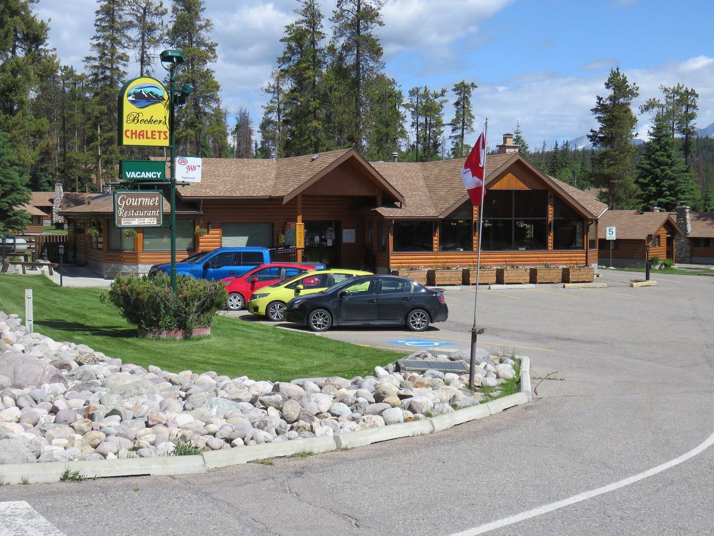 Becker's Chalets Jasper met geparkeerde auto's en een Canadese vlag langs een grindweg in een dennenbos.