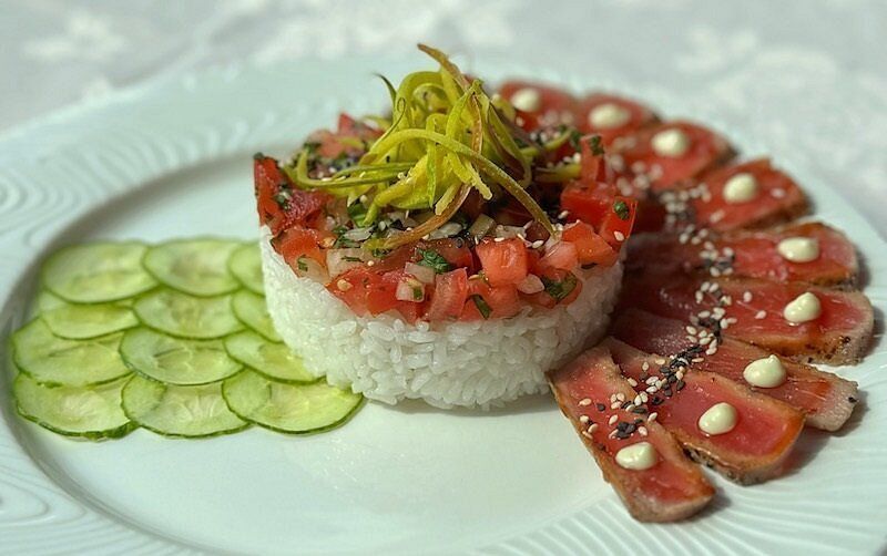 Sushischotel met komkommerschijfjes, tonijnnigiri en een centrale berg tonijntartaar op een wit bord.