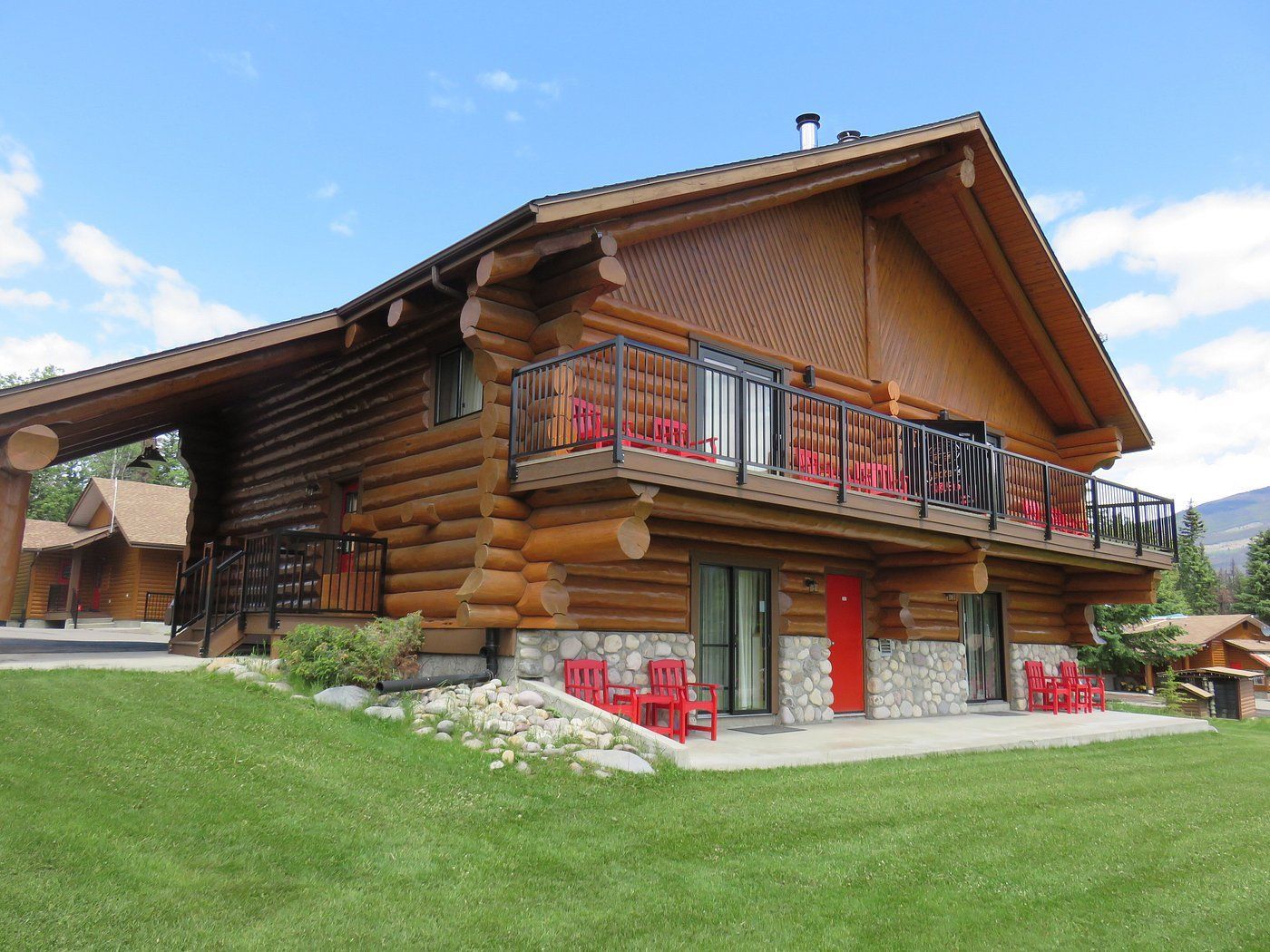 Houten chalet van Becker's Chalets Jasper met rode balkons en een groen gazon onder een blauwe hemel.