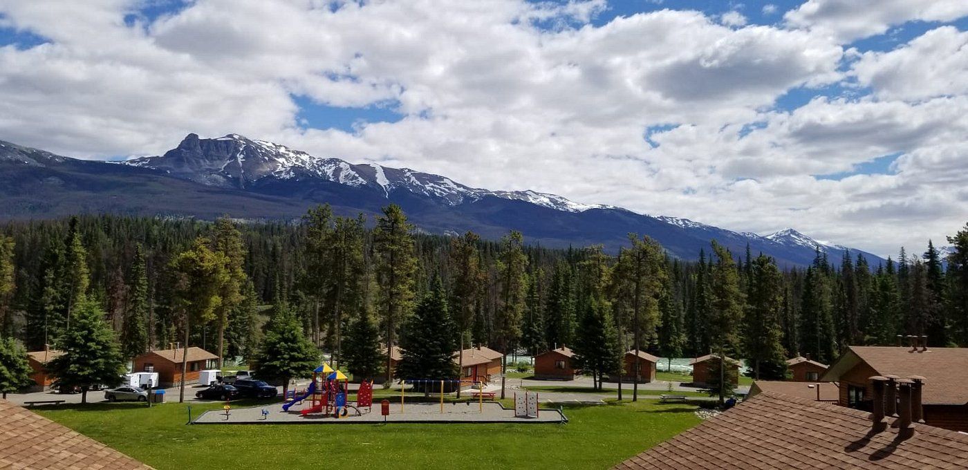 Overzicht van Becker's Chalets Jasper  met een speeltuin, dennenbomen en besneeuwde bergtoppen onder een bewolkte hemel.
