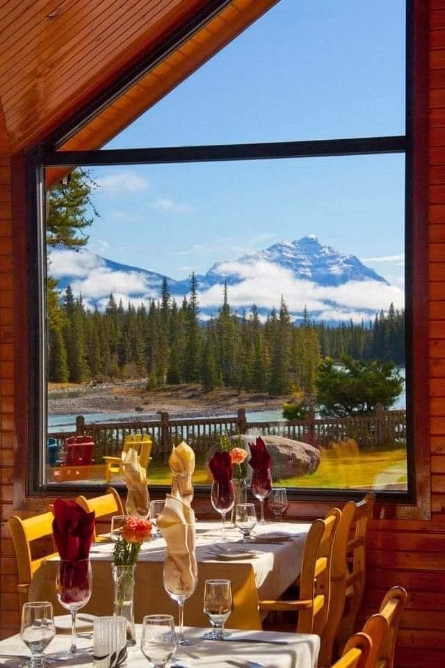 Eetterras van Becker's Chalets Jasper met wijnglazen, met uitzicht op besneeuwde bergen en dennenbomen door een groot raam.