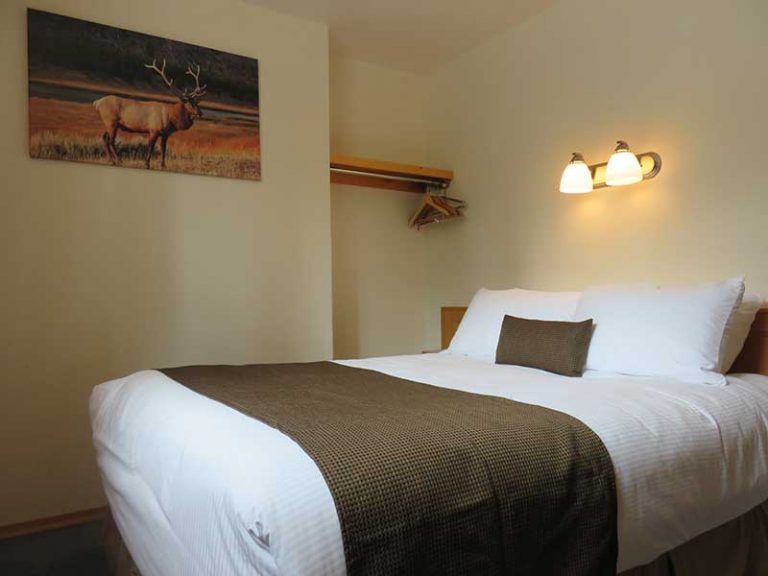 Slaapkamer van Becker's Chalets te Jasper met een opgemaakt bed, muurdecoratie en een brandende lamp boven het kussen.