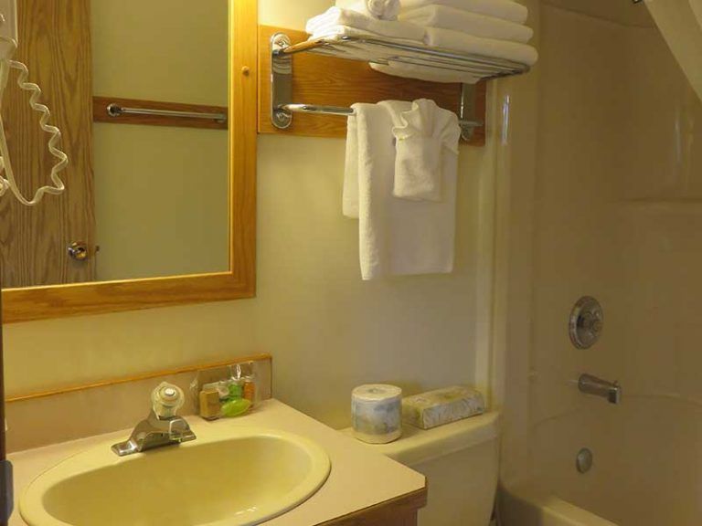 Kleine beige badkamer van Becker's Chalets te Jasper met wastafel, spiegel, handdoekrek, planken en een toilet naast een douchecabine.