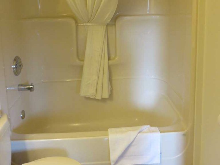 Witte badkuip en douche van Becker's Chalets te Jasper met geel gordijn en handdoek in een betegelde badkamer.
