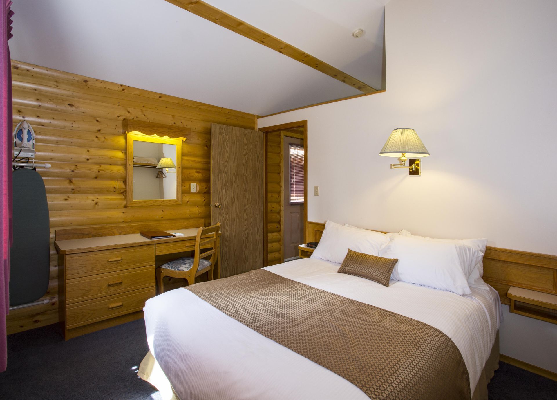 Gezellige slaapkamer met houten lambrisering, wit bed, commode en wandlamp.