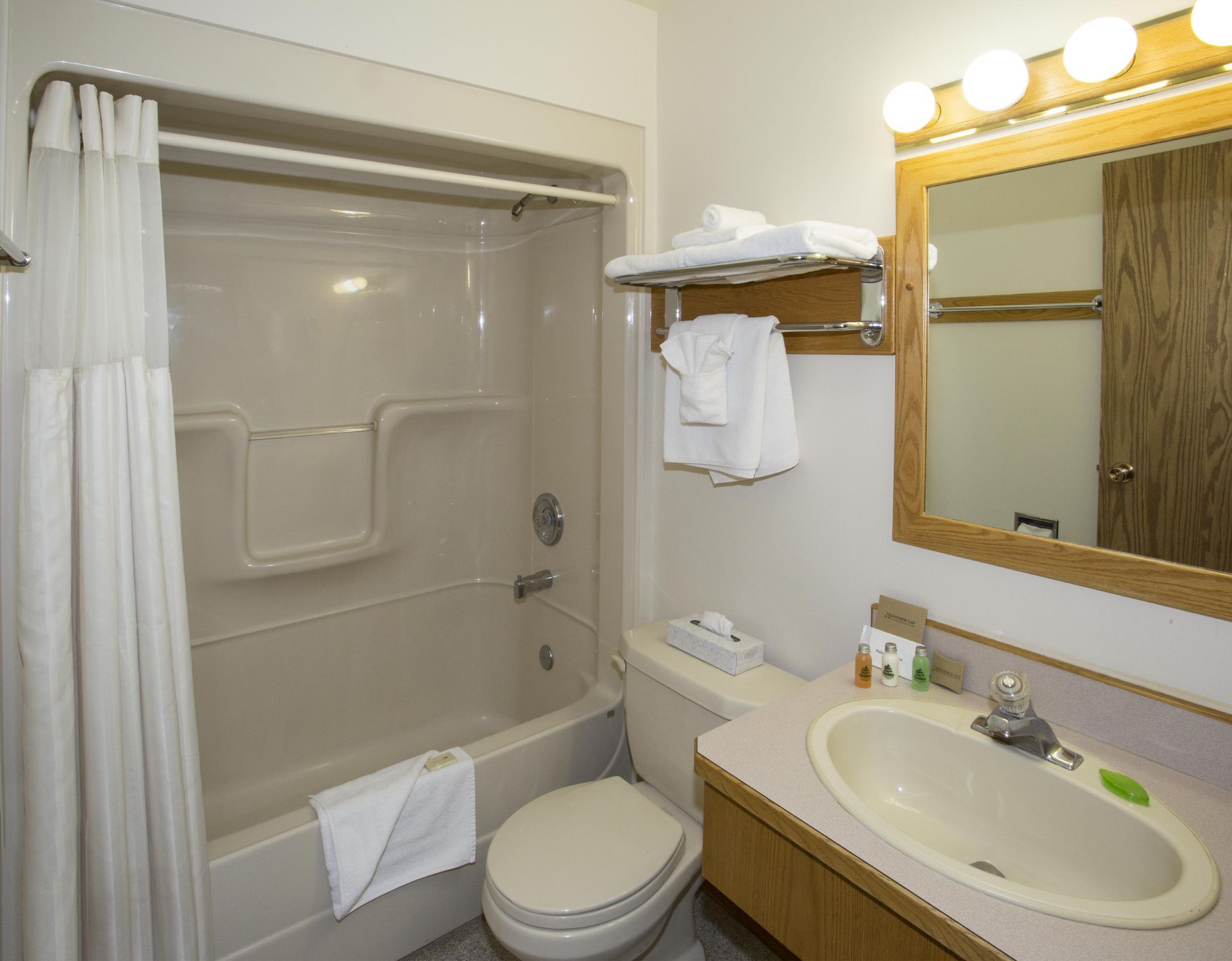 Kleine beige badkamer met douche, toilet, wastafel, spiegel en handdoekrek.