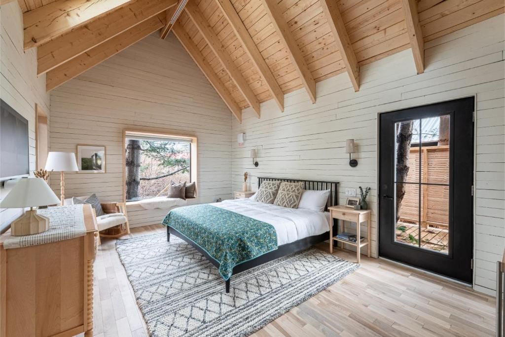 Lichte slaapkamer van Black Forrest Cabins, Mahone Bay met gewelfd houten plafond, turquoise sprei, rieten stoel en grote vensternis.