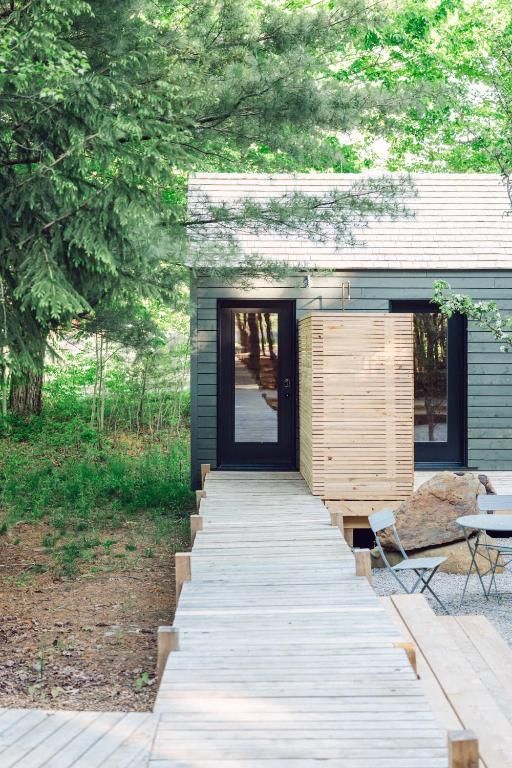 Een houten pad leidt naar een terrasje bij de sauna van Black Forrest Cabins, Mahone Bay, omgeven door groene bomen en tuinstoelen.