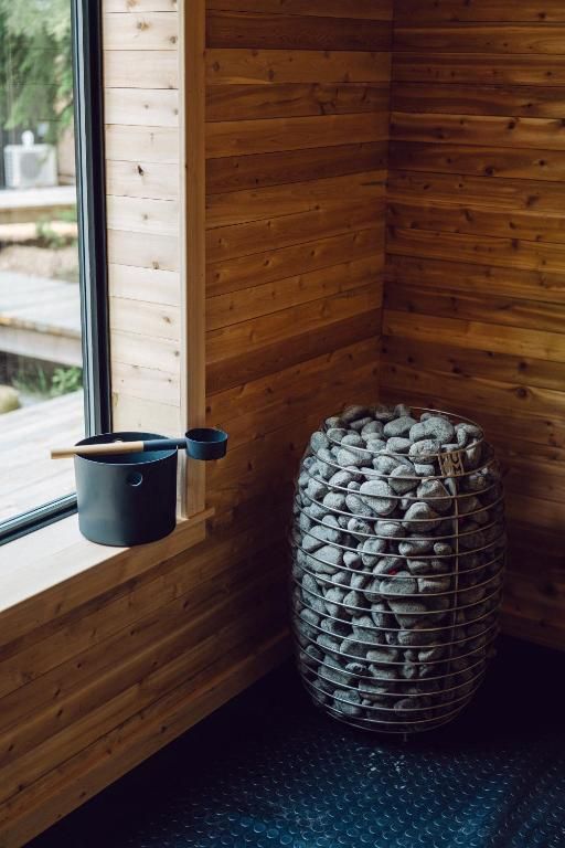 Een saunahoek in de sauna van Black Forrest Cabins, Mahone Bay met houten lambrisering, een hangende pollepel en een hoge mand met stenen op een donkere vloer.