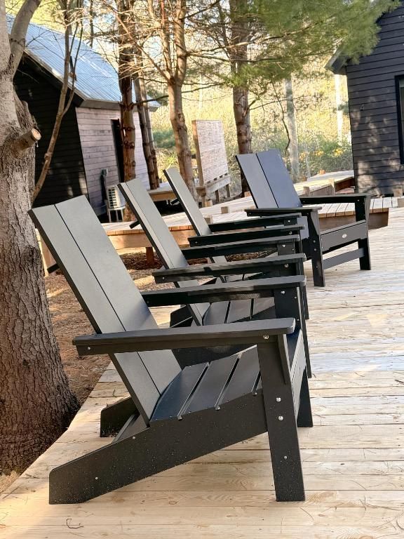Een rij zwarte Adirondack-stoelen op een rustiek terras van Black Forrest Cabins, Mahone Bay tussen bomen en hutten.