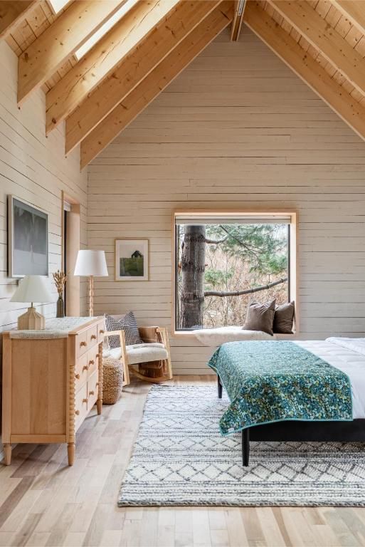 Lichte zolderkamer van Black Forrest Cabins, Mahone Bay met houten lambrisering, een bed, commode, vloerkleed en een grote vensterbank.