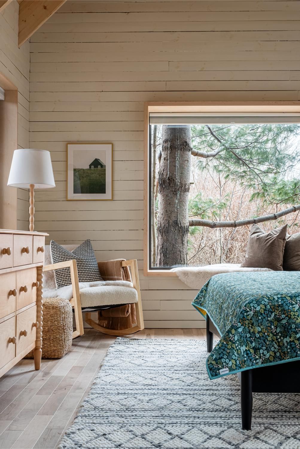 Gezellige slaapkamer van Black Forrest Cabins, Mahone Bay met een groot raam, lichte houten muren, een gevlochten stoel, een commode en blauw beddengoed met patroon.