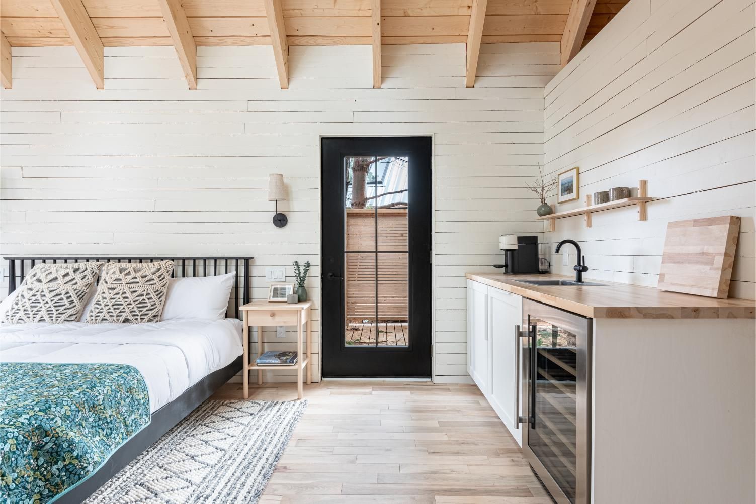 Gezellige witte slaapkamer van Black Forrest Cabins, Mahone Bay met bed, houten plafond, zwarte deur en ingebouwd bureau onder een raam.