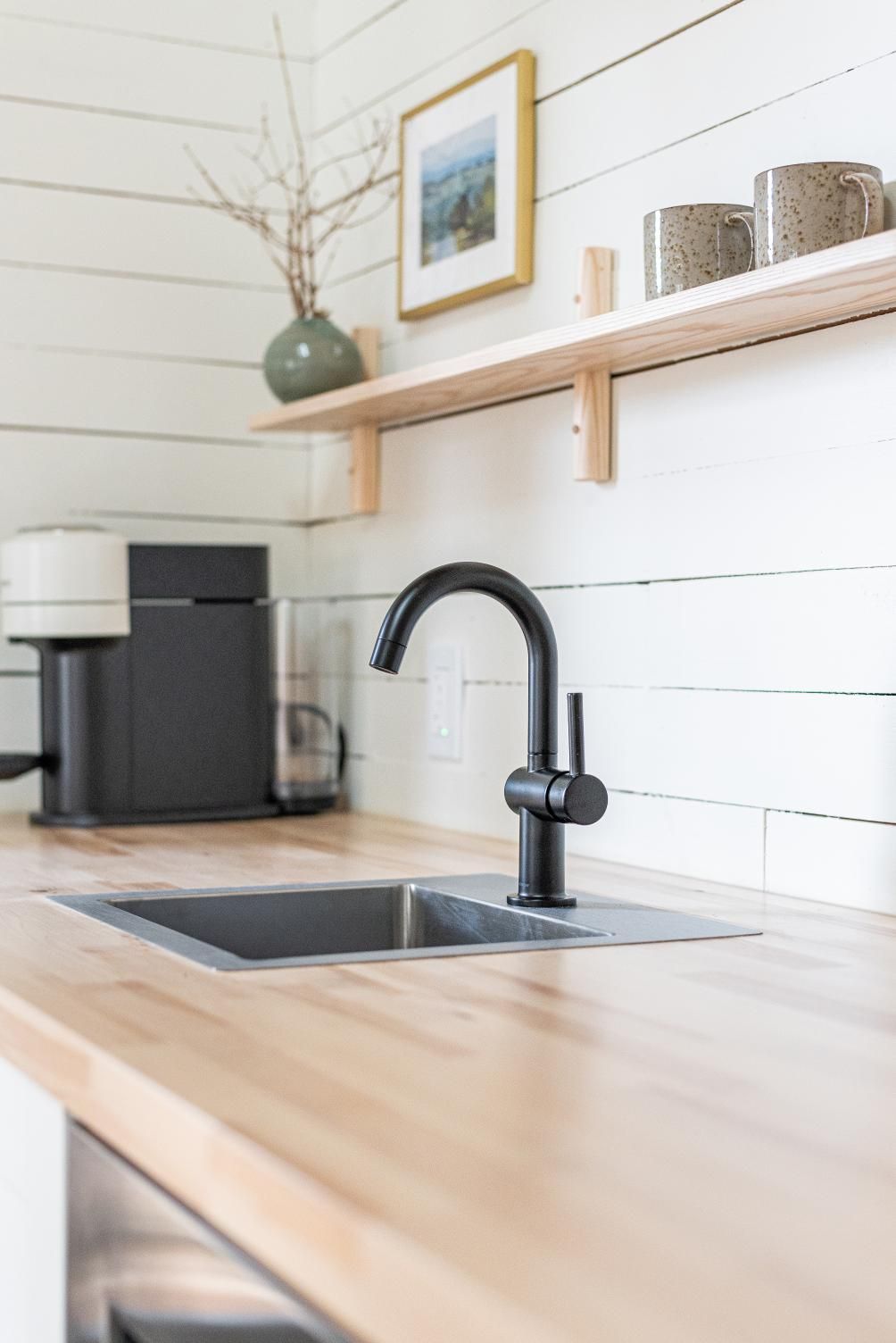 Moderne keuken met spoelbak, zwarte kraan, houten aanrechtblad, koffiezetapparaat en wandplanken in een cabin van Black Forrest Cabins, Mahone Bay.
