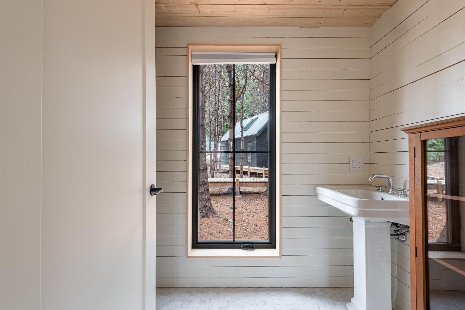 Badkamer met witte houten lambrisering, een smal raam en een witte schoorsteenmantel of plank aan de rechterkant in een cabin van Black Forrest Cabins, Mahone Bay.