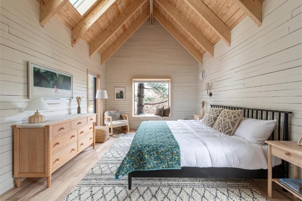Lichte, rustieke slaapkamer van Black Forrest Cabins, Mahone Bay met houten lambrisering, gewelfd plafond, bed, commode en groot raam.
