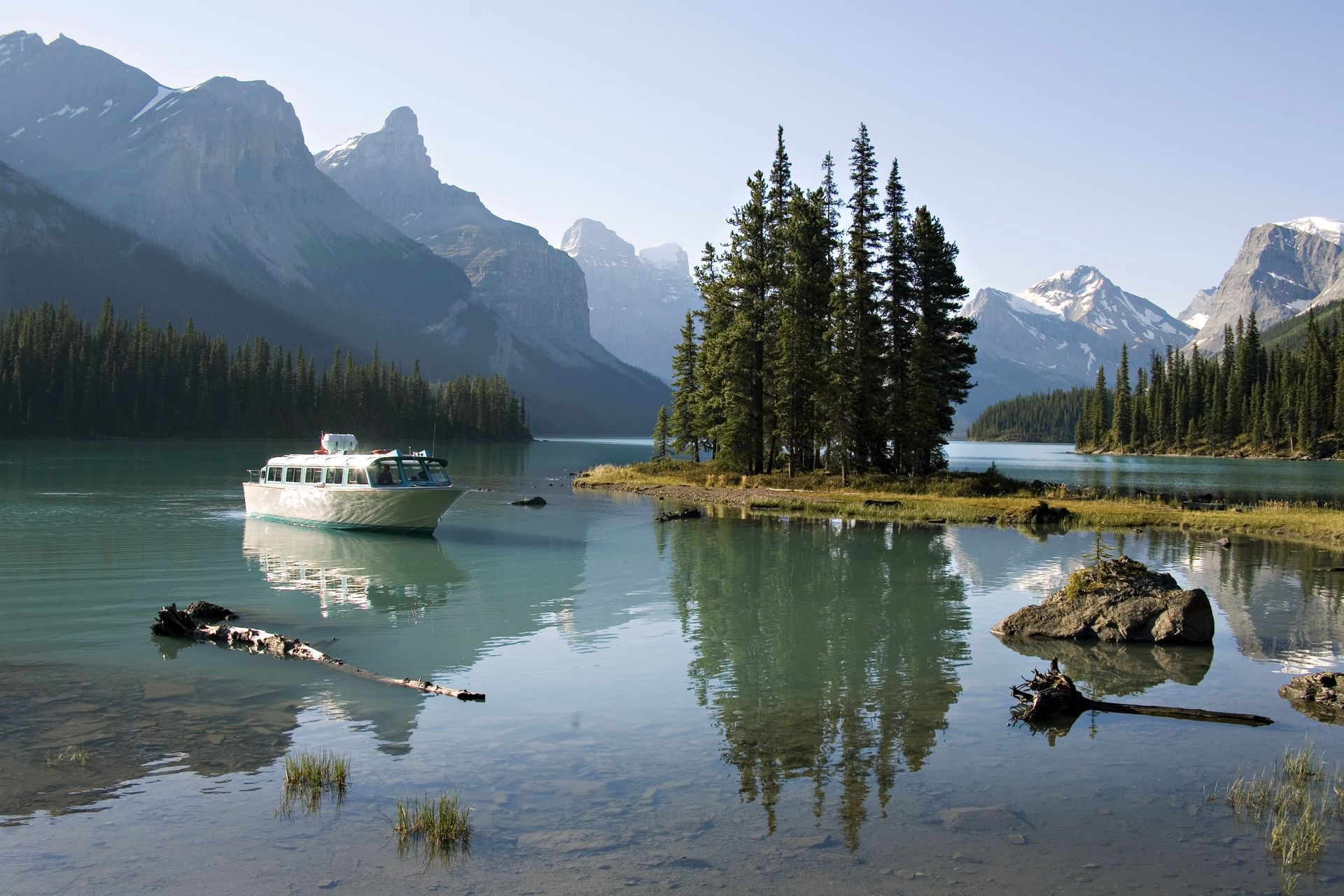 Maligne Lake in Jasper National Park met een klein eilandje van naaldbomen en een boot op het kalme, spiegelende water.