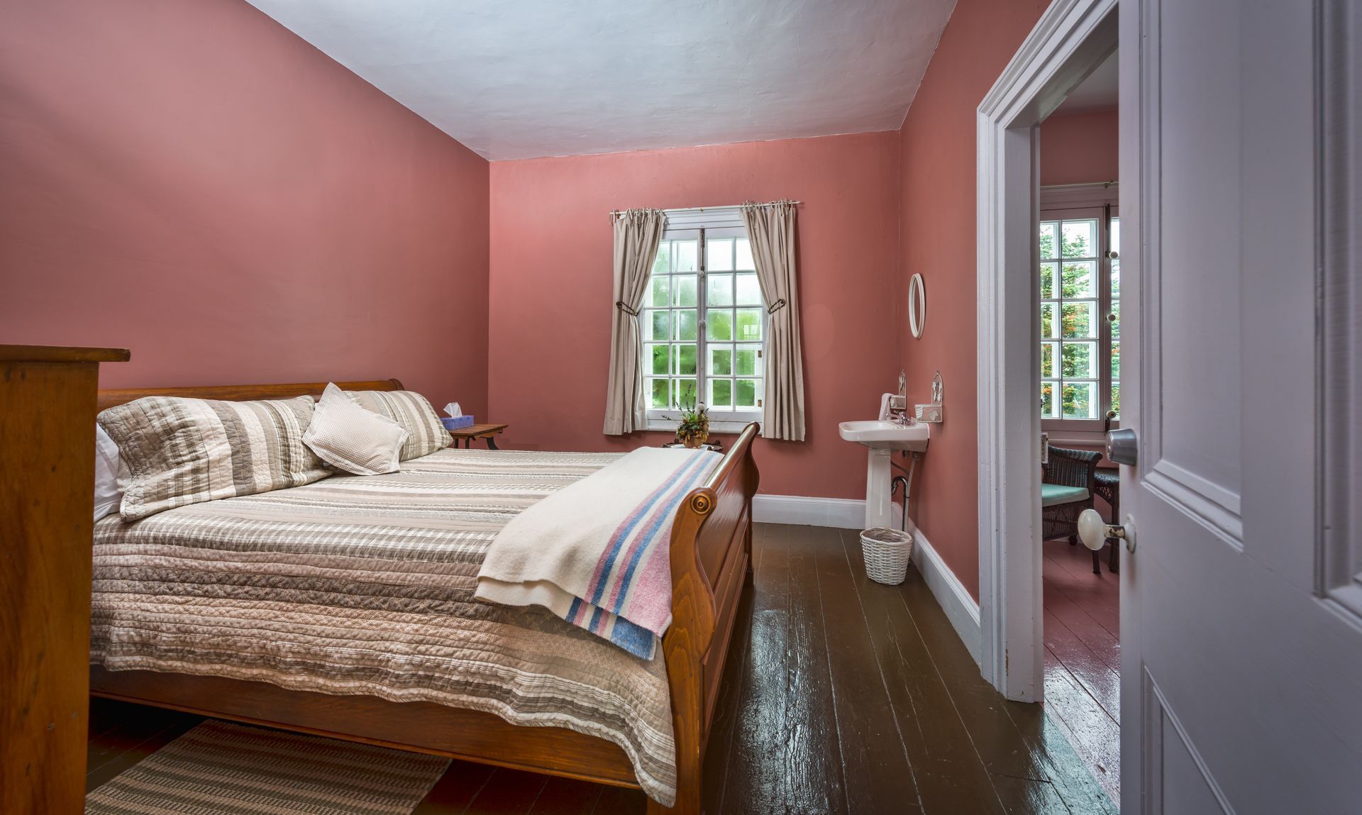Roze slaapkamer met houten bed, wit beddengoed, raam en spiegeldeuren voor de kledingkast.
