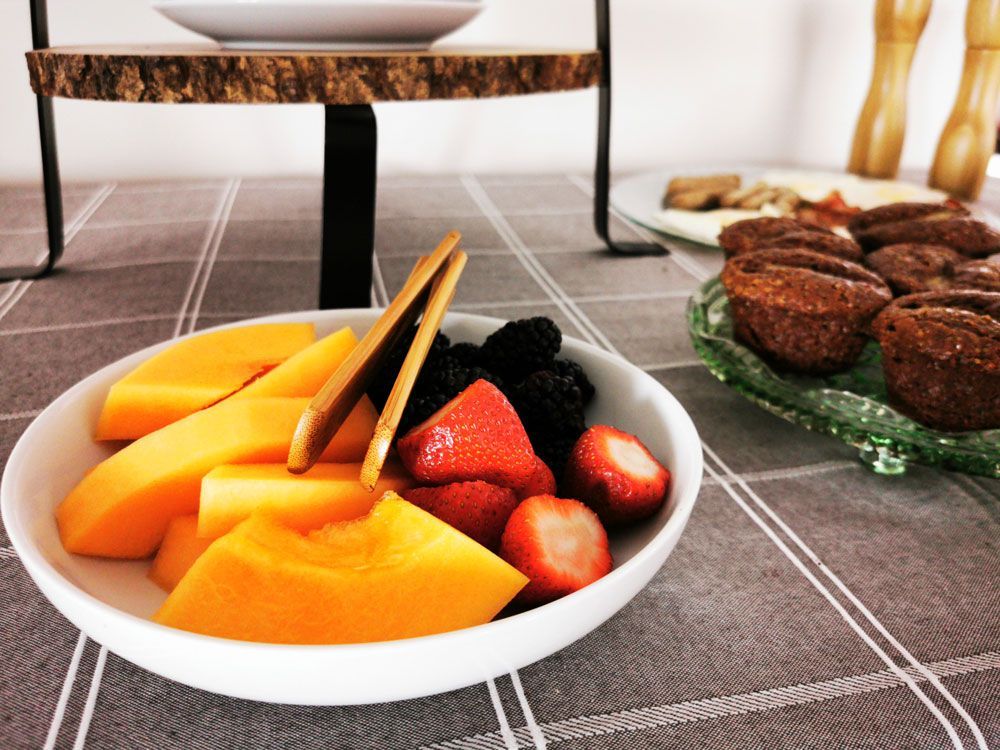 Een schaal met gesneden mango, aardbeien en bramen staat op een tafel naast brownies en een taartplateau.