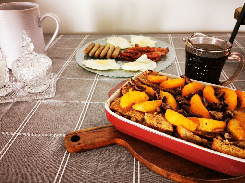 Gekookte groenten in een rode ovenschaal op een tafel, met een bord met eten en mokken op de achtergrond.