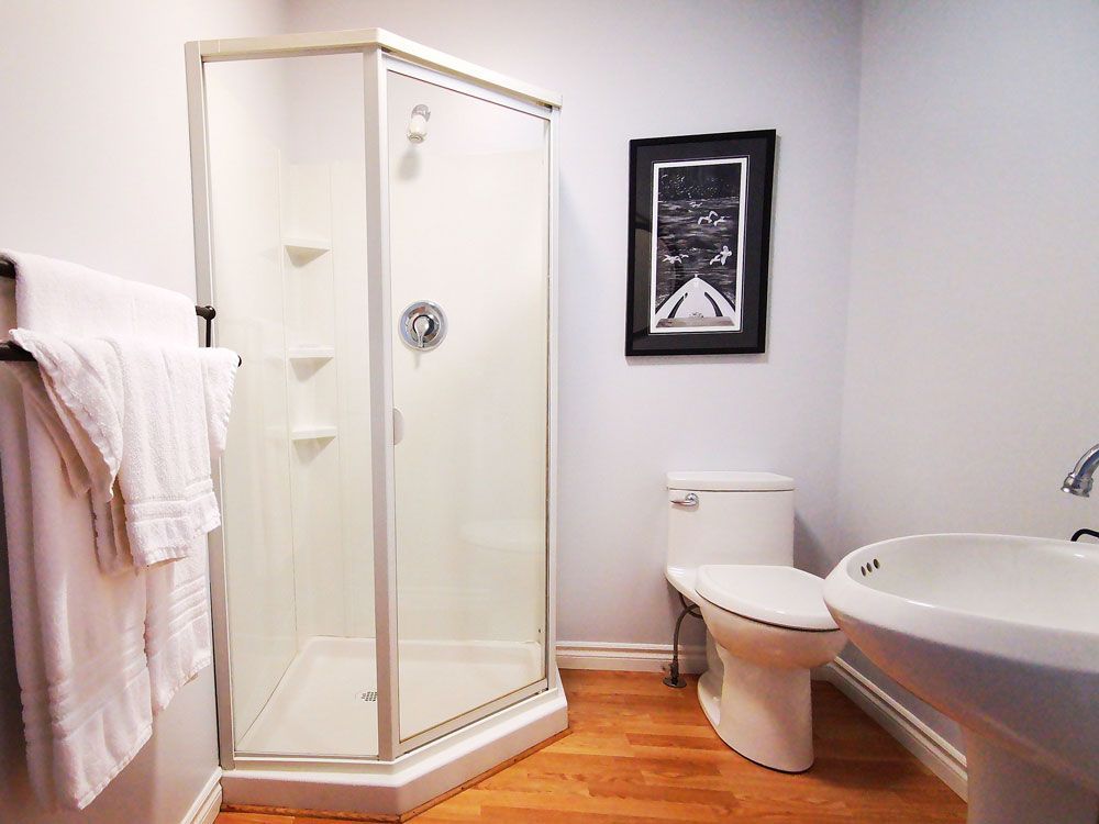 Badkamer met glazen douchecabine, toilet, wastafel en witte handdoeken op een rek.