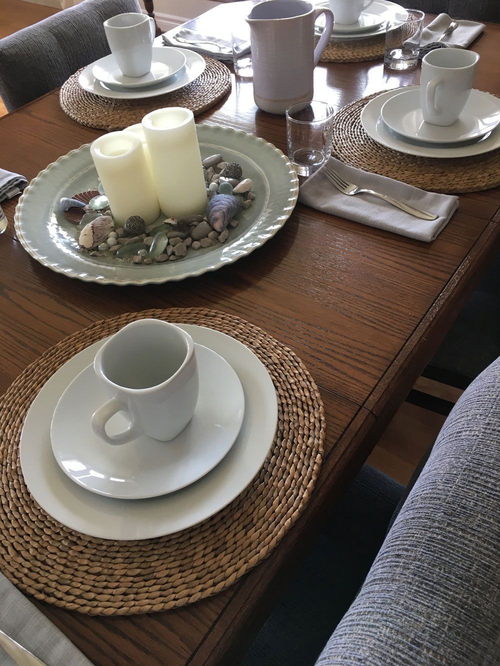 Dek de eettafel met witte kopjes, schotels, kaarsen en placemats op een houten tafel.